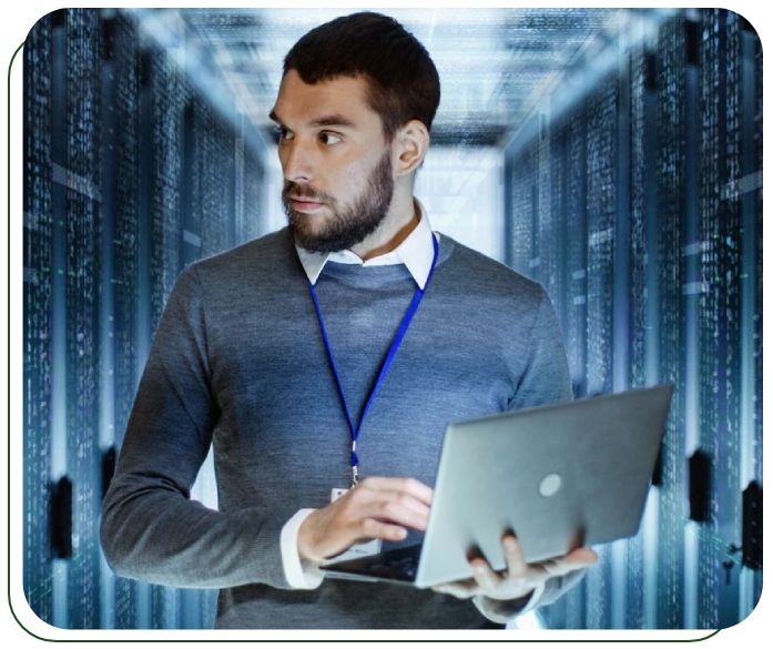 A man holding a laptop in front of a server room.