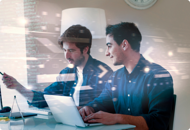 Two men sit at a desk working together on a laptop, with digital graphics and code overlays suggesting collaboration on a technology or software project.